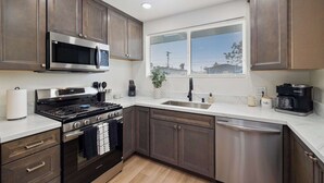 A modern kitchen with dark wood cabinets, stainless steel appliances, a window with blinds, and a coffee maker on the counter. - 4 Miles to Beach Central and Newly Renovated (San Diego)