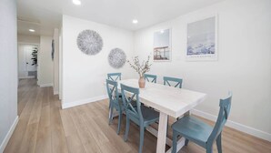 A dining area with a white table and blue chairs, a vase with branches, and two wall decorations. - 4 Miles to Beach Central and Newly Renovated (San Diego)