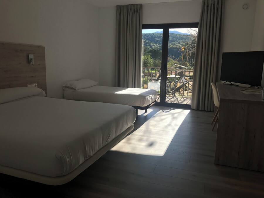 A hotel room with two beds, a desk, and a view of a balcony with outdoor furniture.