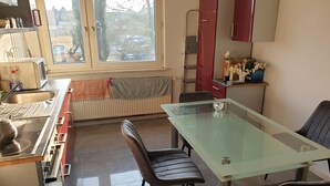 Una cocina moderna con una mesa de vidrio para comer, dos sillas, una estufa y una ventana con vista a la calle.