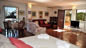 A well-lit room with a bed, a sofa, a dining table with chairs, and a television on a stand. - Casa Marta With Garden and hot tub (Formia)