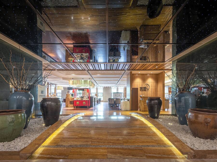 A modern hotel lobby with a wooden floor, large vases, and a central walkway.