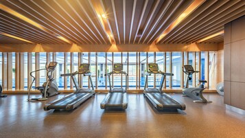 Un gimnasio con cintas de correr, elípticas y un amplio ventanal con vistas a una piscina.