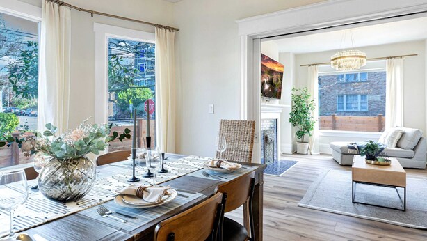 Un comedor con mesa de madera dispuesta para cuatro, un florero con flores y vistas a la ciudad a través de amplias ventanas.