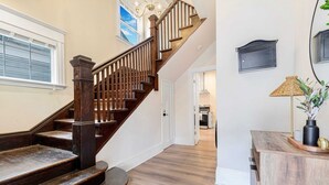 Una escalera de madera con barandilla, una pared blanca con un cuadro y un armario de madera con una lámpara.