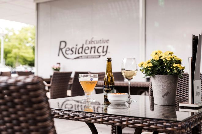 A table with a bottle, a glass, and a flower arrangement.