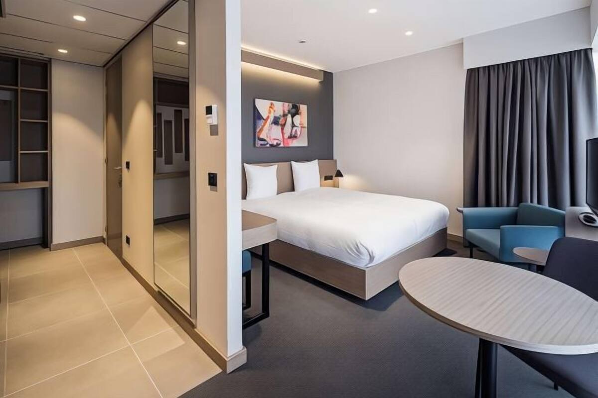 Quarto de hotel moderno com cama, mesa de cabeceira e uma pequena mesa redonda.