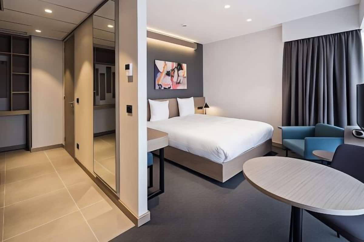 Quarto de hotel moderno com cama, uma mesinha, um sofá e um espelho grande.