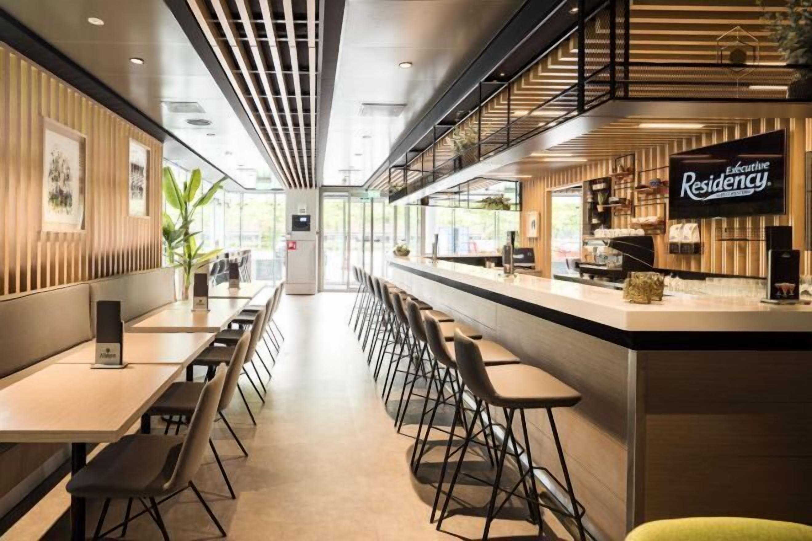Een moderne hotellobby met een lange receptiebalie, een zithoek en een trap naar een hoger niveau.