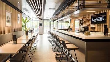 Een moderne hotellobby met een lange receptiebalie, een zithoek en een trap naar een hoger niveau.
