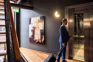 Ein Mann in einem Anzug steht in einer Diele mit einem Gemälde an der Wand und einer Aufzugtür.