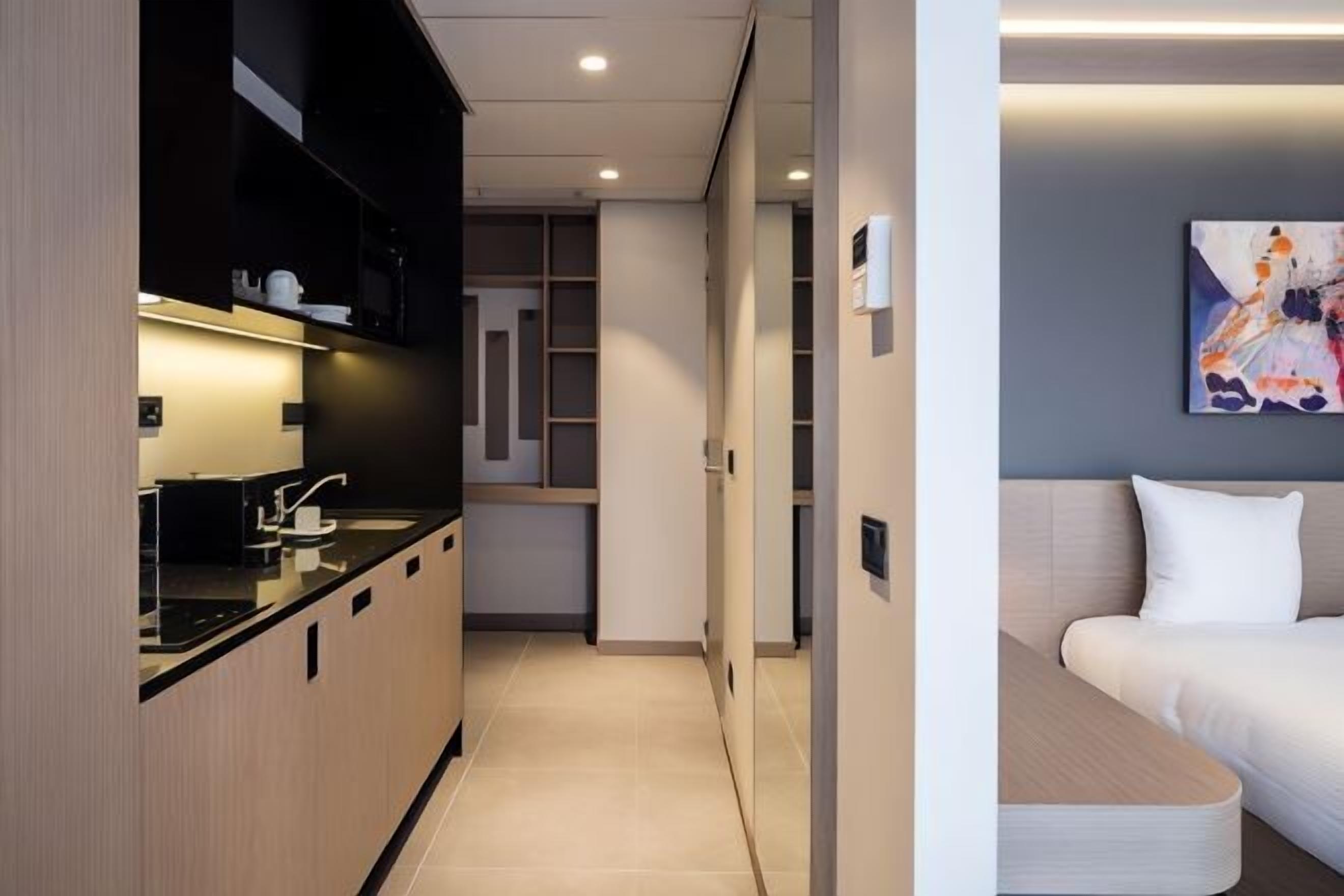 A modern hotel room with a kitchenette, a sofa, and a painting on the wall.
