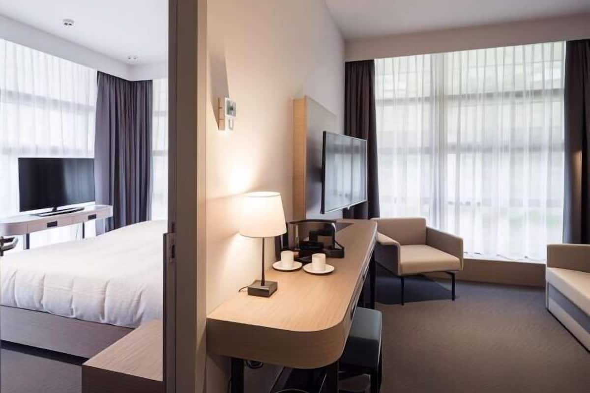 Quarto de hotel moderno com uma cama, uma mesa com abajur, uma televisão e um sofá.