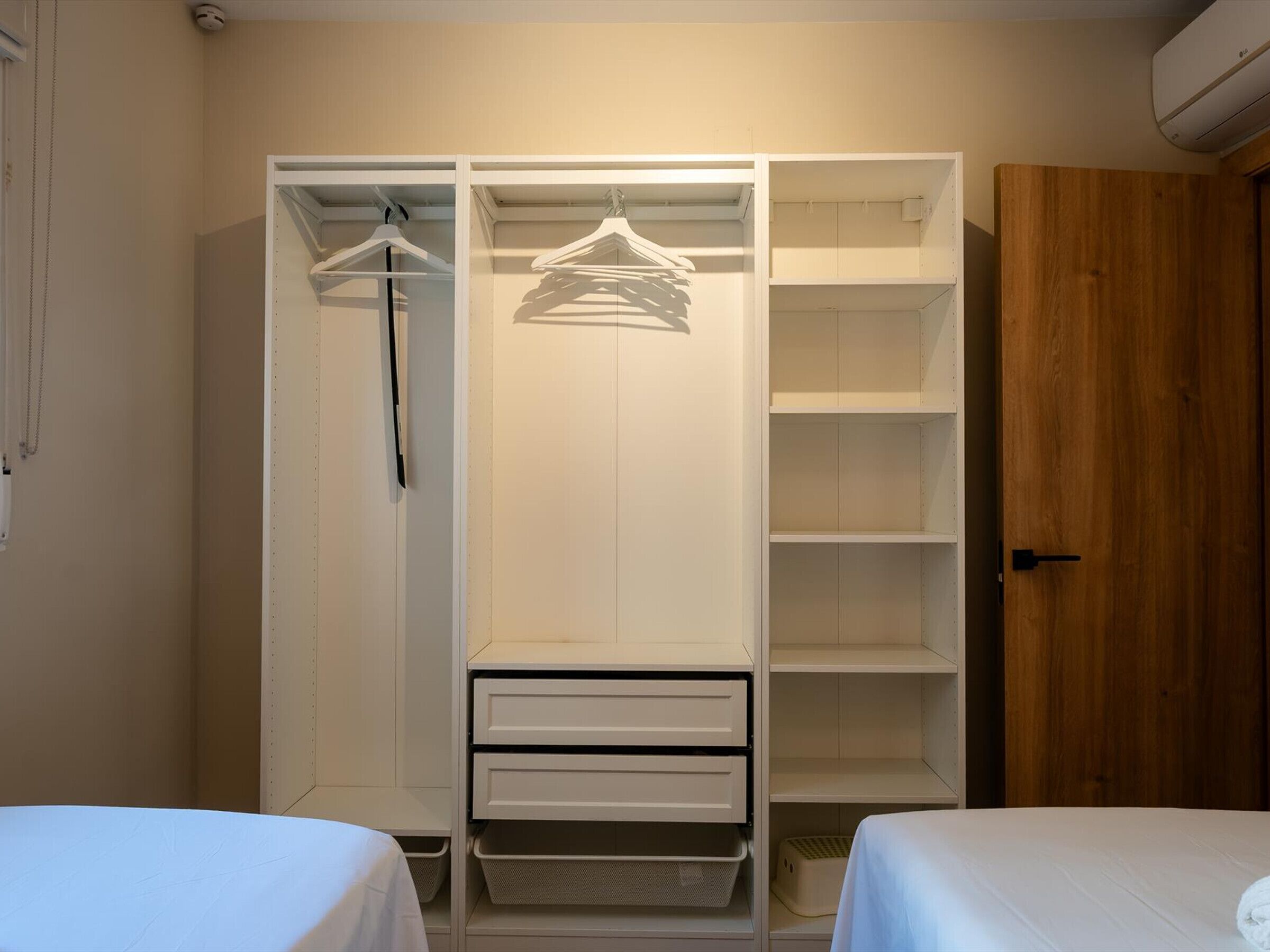 Een slaapkamer met een kledingkast, twee bedden en een houten deur.