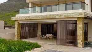 A modern two-story house with a glass balcony, a covered outdoor seating area, and a swimming pool.