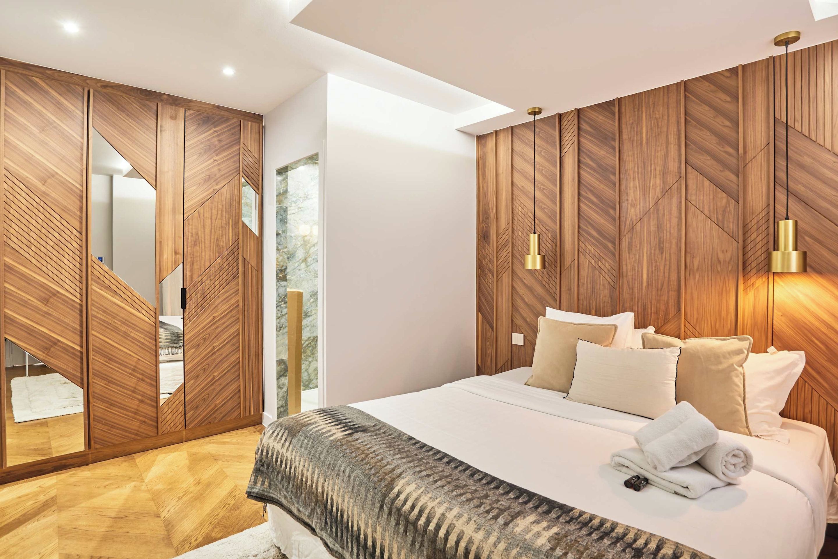A modern bedroom with a large bed, wooden wardrobe, and a mirror.