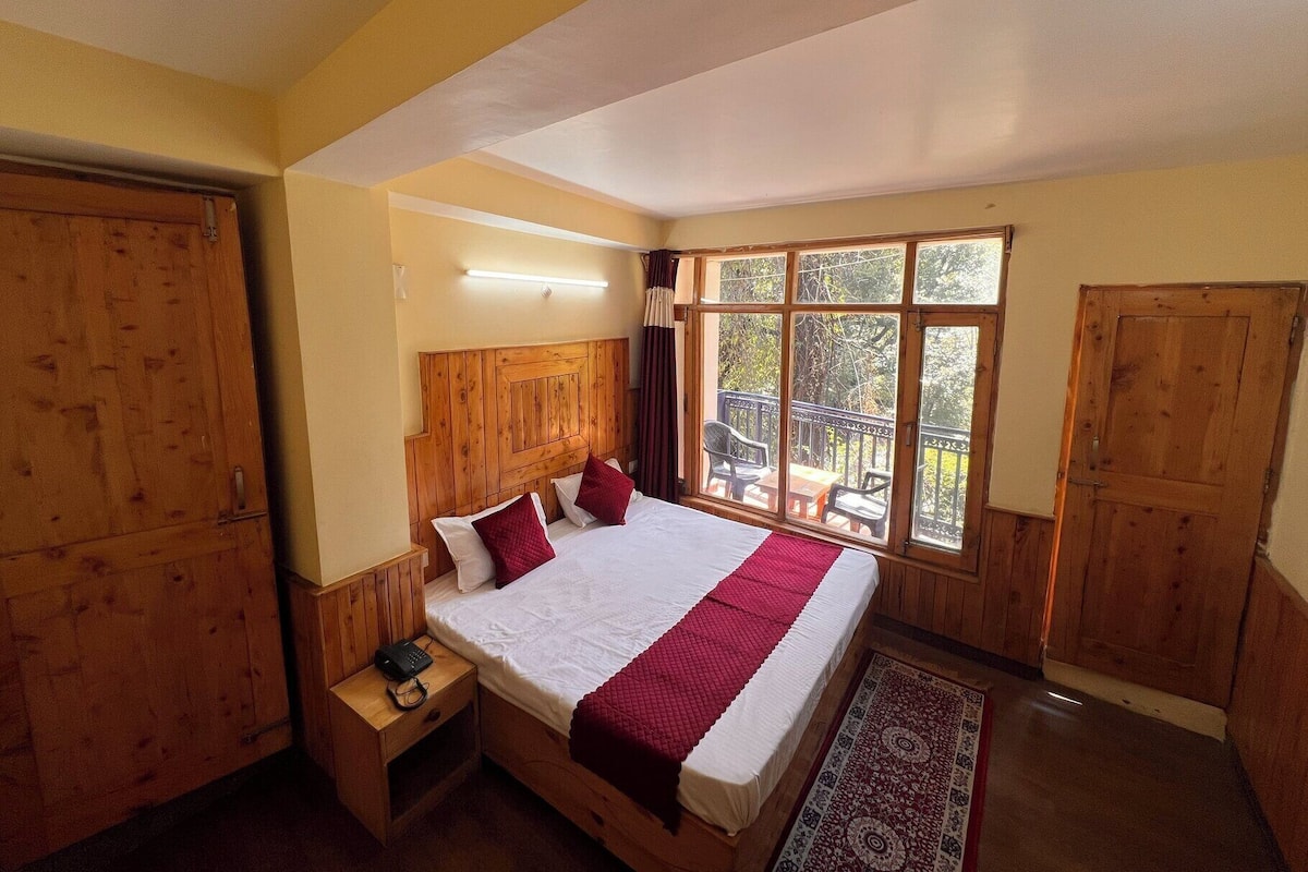 Un dormitorio con una cama grande, cabecera de madera, una mesita de noche con un teléfono y una ventana que ofrece vistas a árboles.