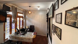 A room with a wooden dining table, a black office chair, a hanging light fixture, and framed pictures on the wall. - Holiday Moods (Manali)