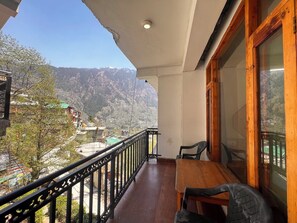 Un balcon avec une table et des chaises en bois, donnant sur un paysage montagneux où l’on aperçoit des bâtiments au loin.