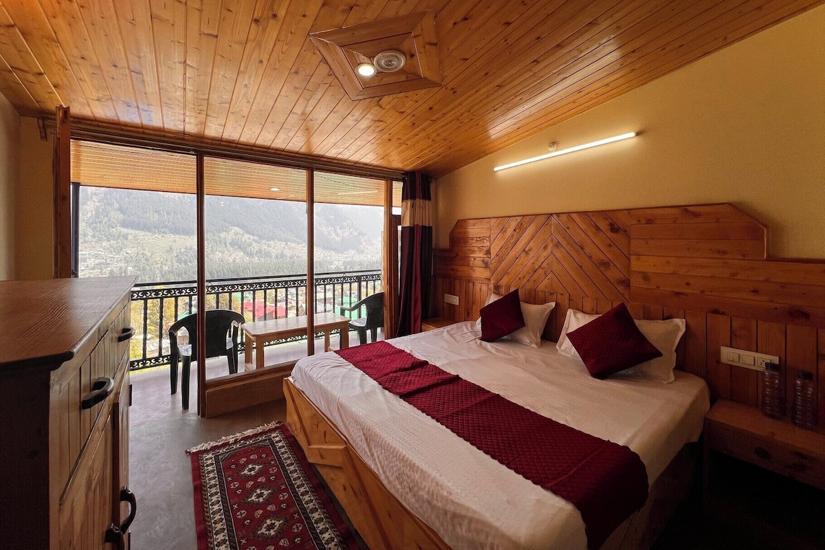 Un dormitorio con paneles de madera, una cama grande, un escritorio y un balcón con vistas a las montañas.