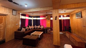A cozy room with a wooden ceiling, a sofa set, a dining table, and curtains. - Holiday Moods (Manali)