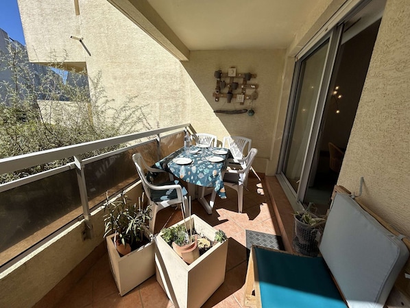A balcony with a table and chairs, potted plants, and a sliding glass door.
