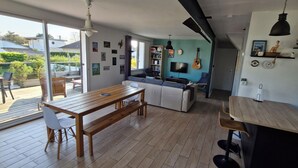 A modern kitchen with a wooden table and bench, a built-in seating area, and a large window overlooking a garden. - House 300 m from the beach!  Close to Cabourg, ideal for families. (Varaville)