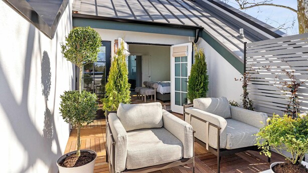 Un espace de vie extérieur moderne, comprenant un canapé et des fauteuils, une petite table et des plantes en pot.