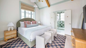 Une chambre à coucher comprenant un lit, des tables de chevet, une commode, une commode en bois et une porte donnant sur une salle de bain.