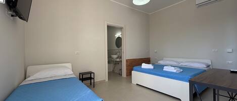 A hotel room with two beds, a small table, a TV mounted on the wall, and an air conditioning unit.