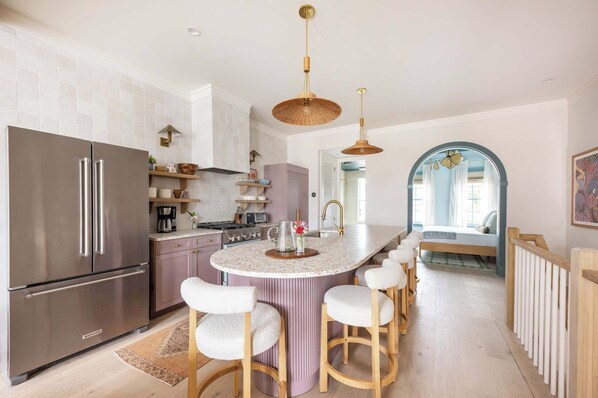 A modern kitchen with a central island, stainless steel appliances, and a breakfast bar with stools. - Chic 4bd Downtown Home w/ Rooftop (Charleston)
