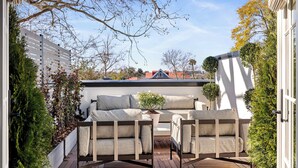 Une terrasse avec une plateforme en bois, un espace salon extérieur comprenant deux canapés et des fauteuils, et une plante en pot.