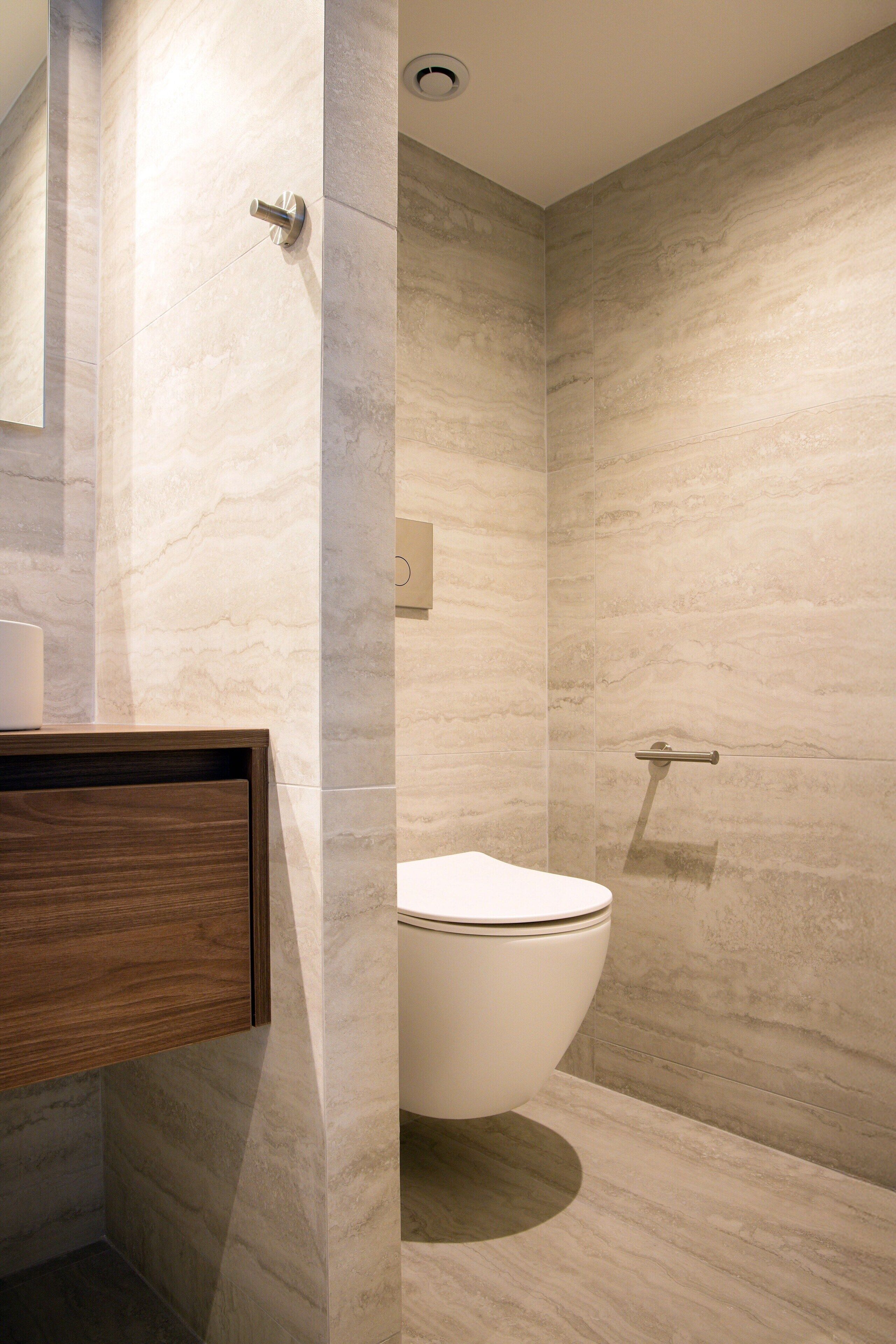A modern bathroom with a marble wall, a wooden vanity, and a white toilet.