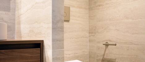 A modern bathroom with a marble wall, a wooden vanity, and a white toilet.