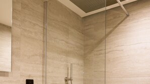 A modern bathroom with a glass-enclosed shower, a wooden vanity, and a marble-tiled wall.