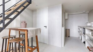 A modern kitchen with a white interior, a wooden staircase, and a small dining area with stools. - Charming AC Duplex - Bastille Le Marais (Paris)