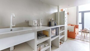 A modern kitchen with a large white sink, built-in shelves, and a countertop with various appliances. - Charming AC Duplex - Bastille Le Marais (Paris)
