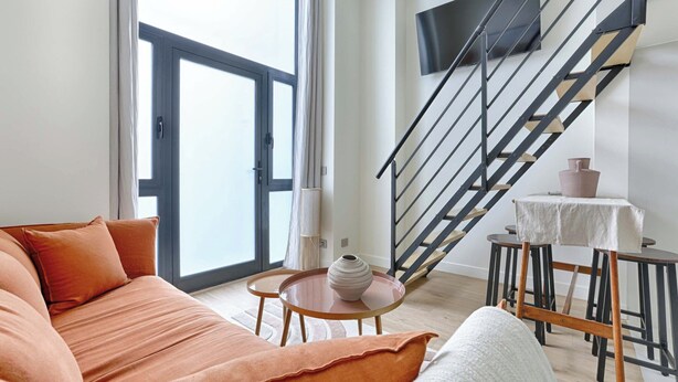 A modern living room with a sofa, a coffee table, and a staircase. - Charming AC Duplex - Bastille Le Marais (Paris)