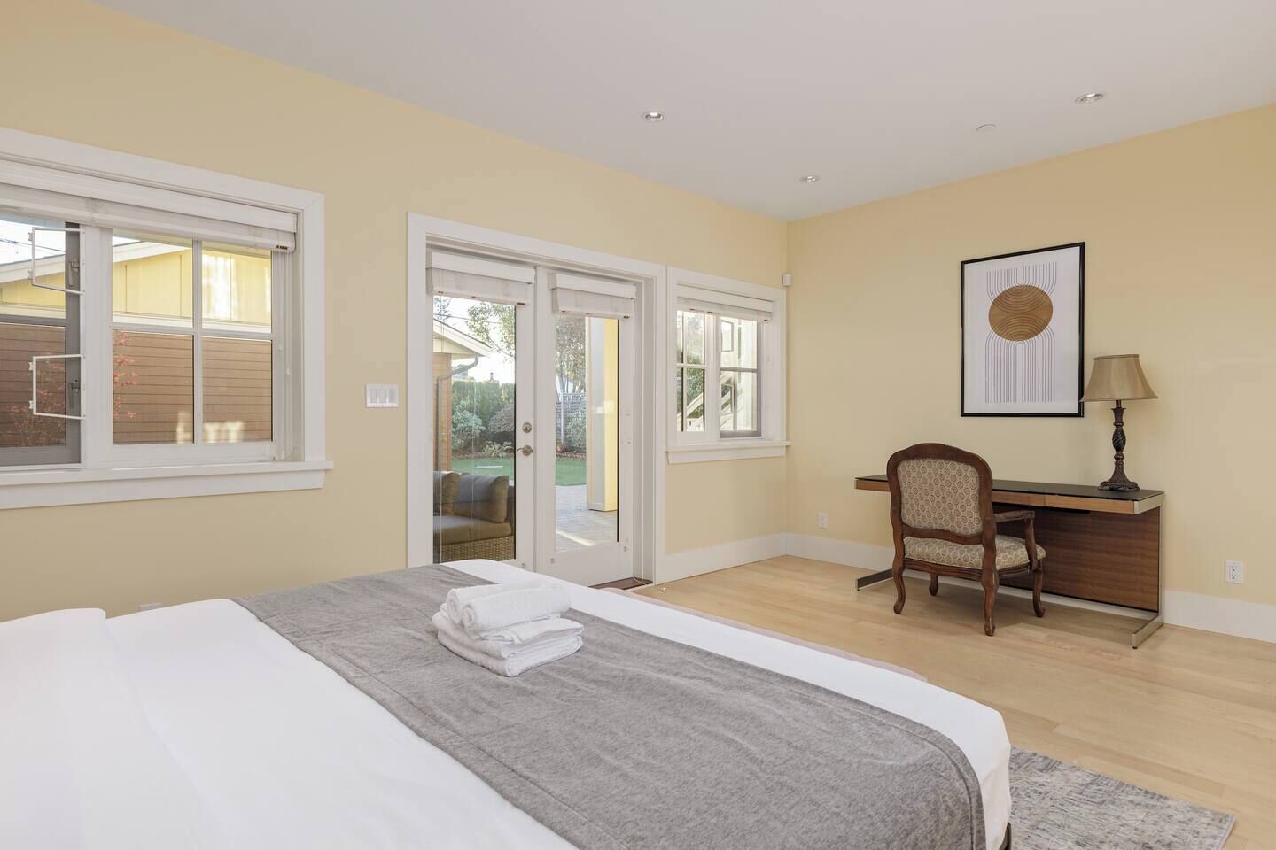 Un dormitorio con cama, escritorio y silla. Hay dos ventanas y una puerta que da a un balcón.