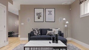 A modern living room with a grey sofa, a white coffee table, and two framed artworks on the wall.
