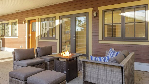 An outdoor patio with wicker furniture, a fire feature, and large windows.