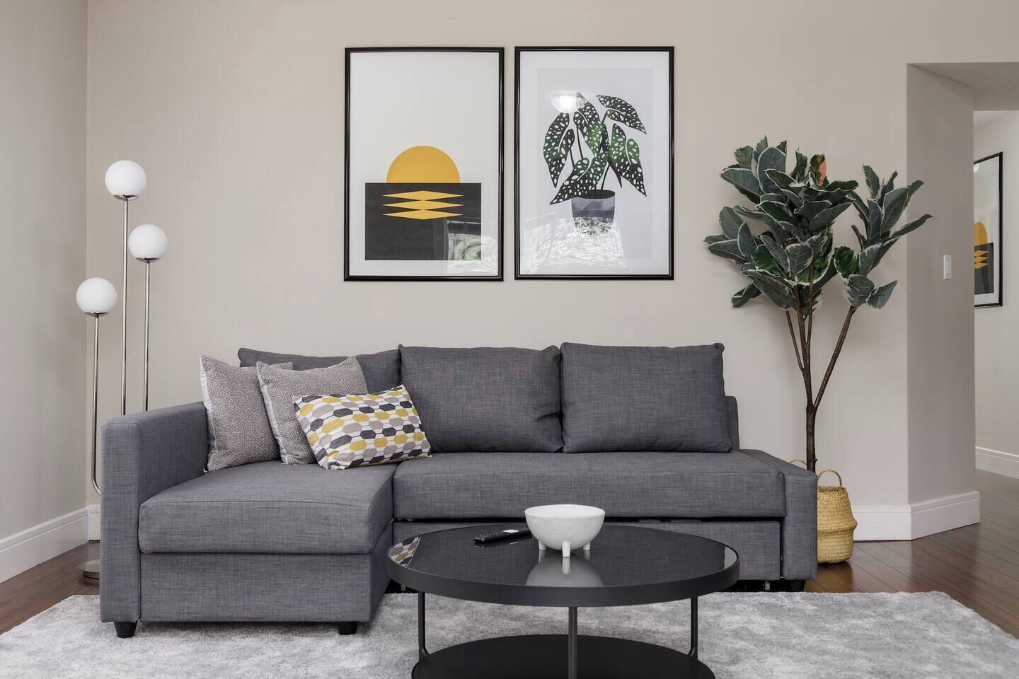 Een moderne woonkamer met een grijze hoekbank, een ronde salontafel en een grote potplant.