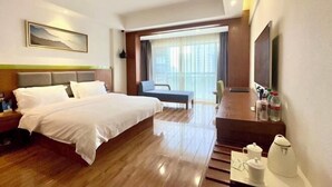 Habitación de hotel con cama, escritorio, silla, televisor y ventana con cortinas.