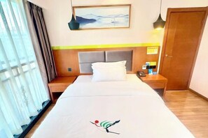 Una habitación de hotel con una cama, una mesita de noche, un cuadro en la pared y una puerta.