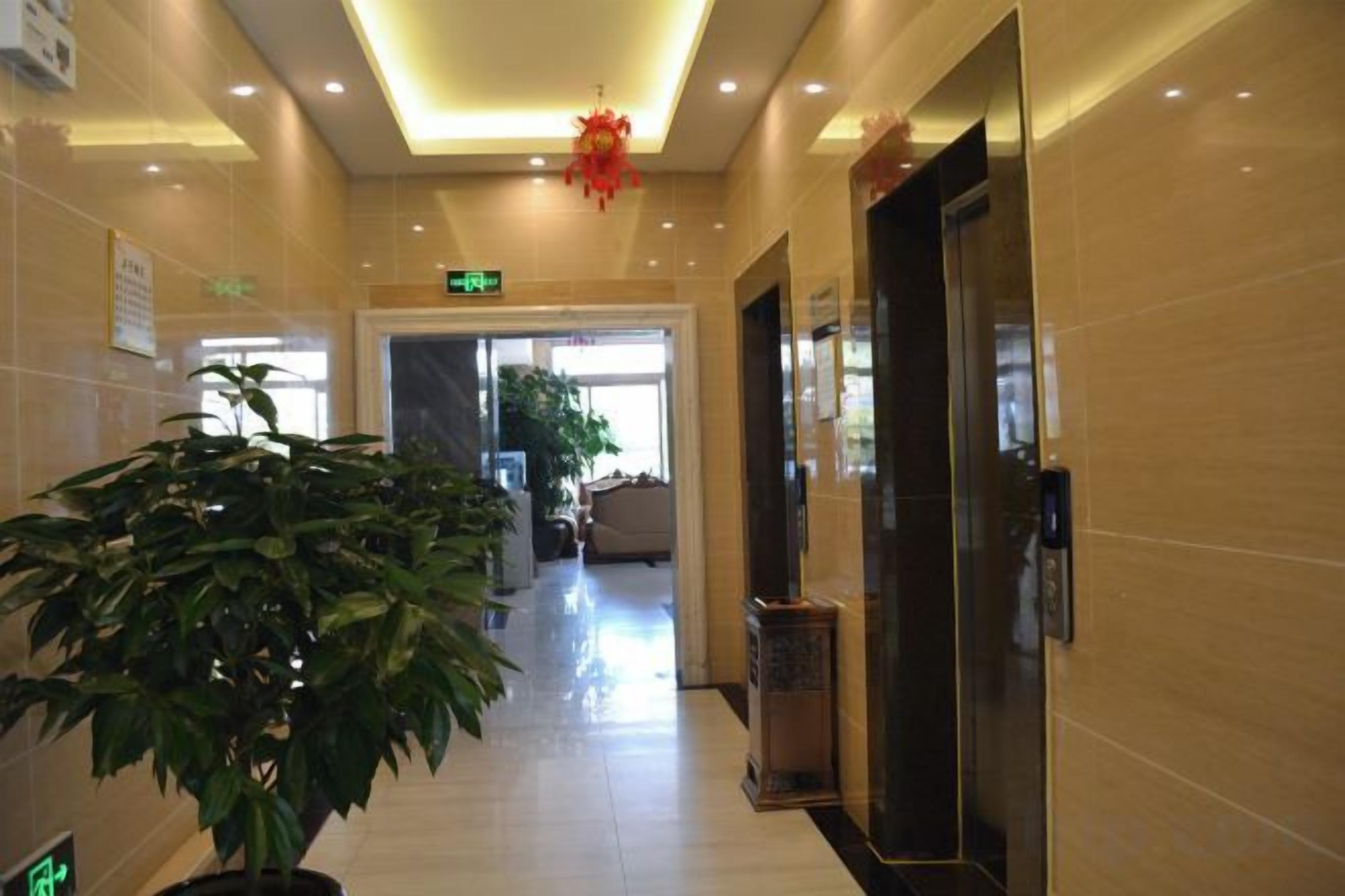 A hotel lobby with a reception desk, a potted plant, a trash bin, and a door leading to another room.