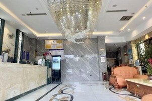 Um hall de hotel com balcão de recepção, um lustre grande, área de estar e piso de mármore.
