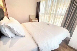 Habitación de hotel con una cama bien hecha, una silla y un ventanal con cortinas.
