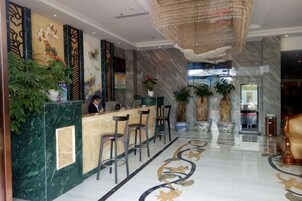 Un vestíbulo de hotel con mostrador de recepción, taburetes de bar, plantas en macetas y un candelabro.