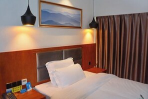 Habitación de hotel con cama, cabecera, mesita de noche con teléfono y tarjeta, un cuadro en la pared y una cortina.