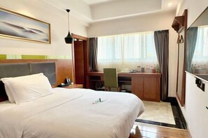 Habitación de hotel con cama, escritorio, silla y un gran ventanal con cortinas.